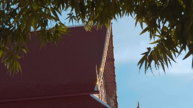 Roofs of traditional Thai style paved with orange tiles and gold carved chofas of the Buddhist Temple in Bangkok. Shot in motion