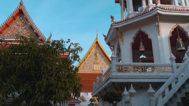 Roofs of traditional Thai style paved with orange tiles, gold carved chofas and the bell tower of the Buddhist Temple in Bangkok. Shot in motion