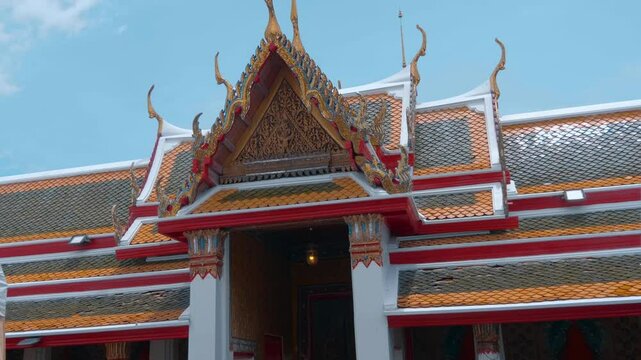 Traditional Lai Thai style orange and blue tiled roof with massive Chofahs (serpent-like edges) and ornate golden carvings of a Buddhist temple in Bangkok. Shot in motion