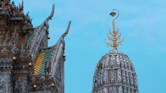 Ancient Buddhist temple (Wat Arun) in traditional Thai architectural style with ornate colorful mosaics and tiles with floral patterns and bells ringing in the wind