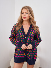 Woman wearing a colorful knit cardigan features a pattern with vivid pink, orange, and purple...