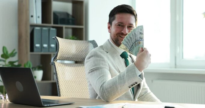 Greedy banker counting money and smiling at table in office
