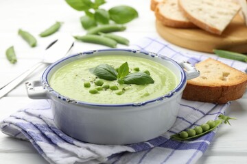 Tasty pea cream soup with basil served on white wooden table, closeup