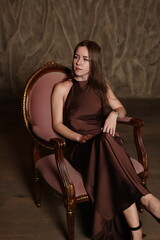 An Elegant Portrait of a Woman Dressed in a Brown Dress Relaxing on a Vintage Chair