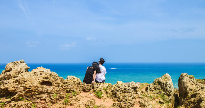 Chinese couple sitting on rocks looking at the coastline scenery oat Longpan Park, Kenting, Taiwan