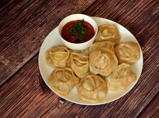 Freshly steamed manti and a cup of tomato spicy sauce with herbs on a wooden table.