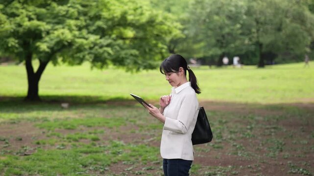 新緑の公園でタブレットを見るビジネスウーマンのサークルショット