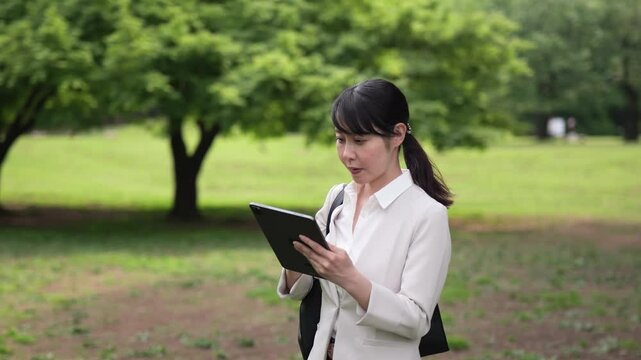 新緑の公園でタブレットを見るビジネスウーマンのドリーインショット - Powered by Adobe