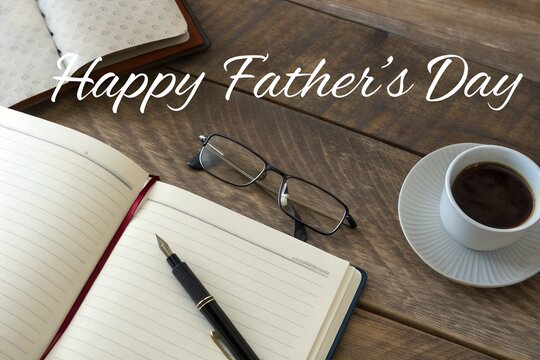 Photo of Father's day scene featuring an open notebook, fountain pen, reading glasses, and a cup of coffee on a rustic wooden table with a greeting message
