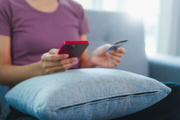 Happy Asian woman sits comfortably on a sofa,smiling while holding multiple credit cards,representing convenient online shopping,smart financial planning,modern digital consumption in a relaxed home