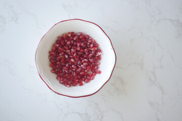 Fresh pomegranate seeds in a bowl on a marble surface
