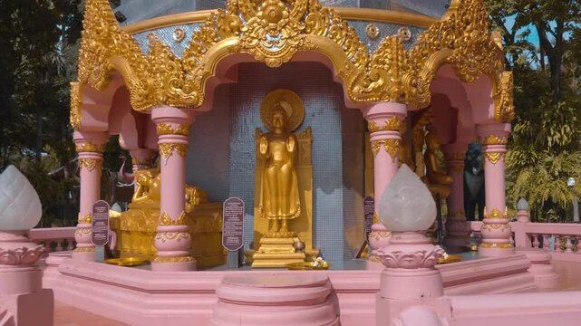 Phra Ket Chulamanee Chedi - an ancient antique Buddhist stupa made of stone and covered in gold stands against the cloudy blue sky and massive trees in the garden of Erawan Museum in Samut Prakan