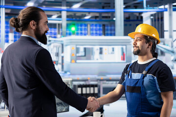 Smiling entrepreneur shaking hands with engineer in solar panel plant after reaching agreement for producing renewable energy. Businessman and worker in photovoltaics factory closing deal