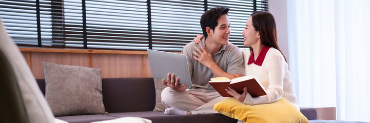 Asian Couple Enjoying Leisure Time with Laptop & Book in Cozy Home Setting Happiness and Relationship Concept with Asian Man and Woman on Sofa