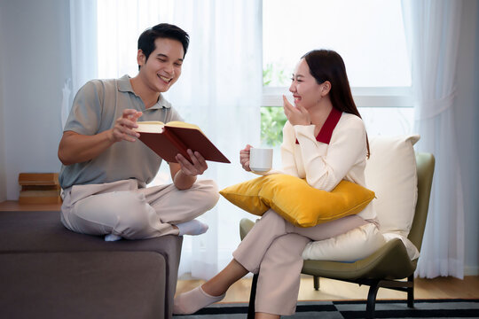 Asian Couple Enjoying Leisure Time Reading Book and Drinking Coffee Together At Home Happy Adult Man and Woman Smiling During Relaxing