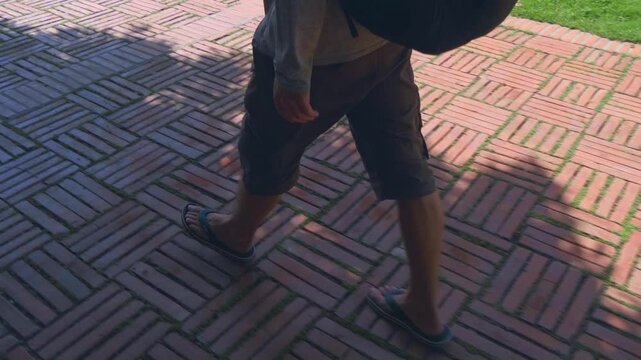 A tourist (farang) with a backpack is walking in flipflops on the red tiles of Wat Mai Chai Wichit temple grounds in Ayutthaya, Thailand. Shot in motion