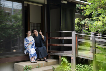 夫婦やカップルでの浴衣での温泉旅行や観光のイメージ　縁側で座る指を差して見つめる広角