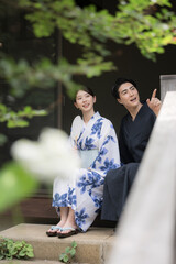 夫婦やカップルでの浴衣での温泉旅行や観光のイメージ　縁側で座る指を差して見つめる　縦　緑の前ボケあり