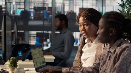General manager reviews financial forecasts with an employee at desk, leading a session on project development and corporate goals. Collaborating to meet business objectives. Camera A.