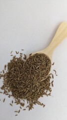 A spoonful of cumin seeds on a white background