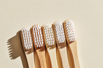 Aesthetic Beige bamboo toothbrushes with white bristles at sunlight on beige background. Simplicity, hygiene, and environmentally friendly alternatives, top view photo, minimal flatlay neutral color