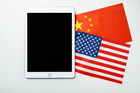 The flags of the USA against China and a tablet with a blank screen. Mockup or copy space. Concept of the United States of America versus China trade war disputes or economic conflict