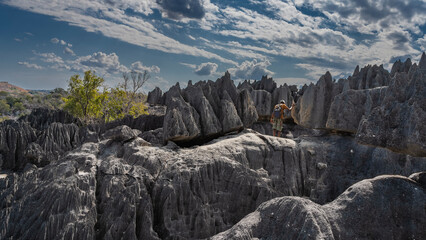 The unique karst cliffs of Madagascar. Sharp peaks, steep furrowed slopes. A man stands on the edge of a cliff, looking down. Back view. Blue sky, clouds. Tsingy De Bemaraha