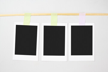 Three blank polaroid photo papers with sticky tape hanging on the rope with a white background. Mockup, template, or copy space. Instant camera photo print frame