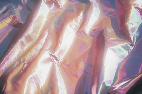 Holographic iridescent background featuring shimmering light on textured folds, creating a captivating display of shifting pastel colors and an ethereal glow