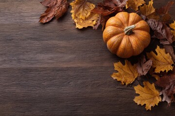 Autumn pumpkin with colorful leaves on a wooden table.