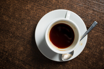 A small cup filled with dark coffee sits on a rustic wooden table, inviting warmth and comfort