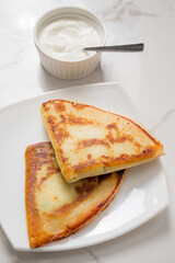 Two golden-brown flatbreads rest on a white plate beside a bowl of yogurt, creating a tempting meal