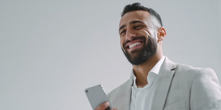 happy middle eastern businessman in light jacket smiles while using smartphone