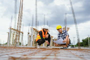 An architect and engineer discuss blueprints on a construction site, wearing helmets, ensuring safety, quality, and progress through collaborative planning.