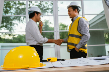 Two architects collaborate at a desk with blueprints, compass, and laptop, planning a construction project with creativity, precision, and teamwork.