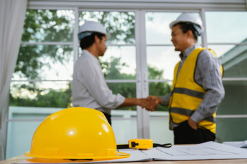 Two architects collaborate at a desk with blueprints, compass, and laptop, planning a construction project with creativity, precision, and teamwork.