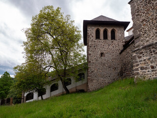 Covered staircase leads to the fortified entrance of Kremnica Castle, passing under trees and beside medieval stone walls and a watchtower, surrounded by lush greenery.