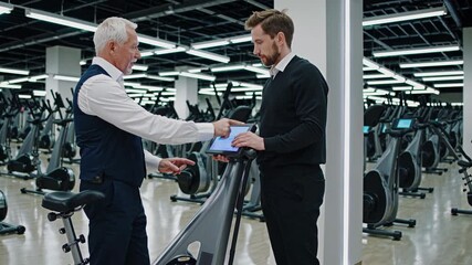 Senior manager discussing exercise bike features with technician - Powered by Adobe