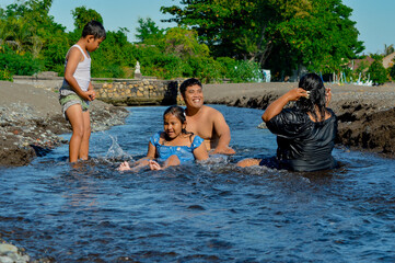 Parents talk casually while their young boy stands nearby, all enjoying the relaxing creek environment together.