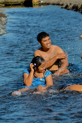 The dad and daughter playfully splash water at each other while enjoying the flowing creek at the beachside.