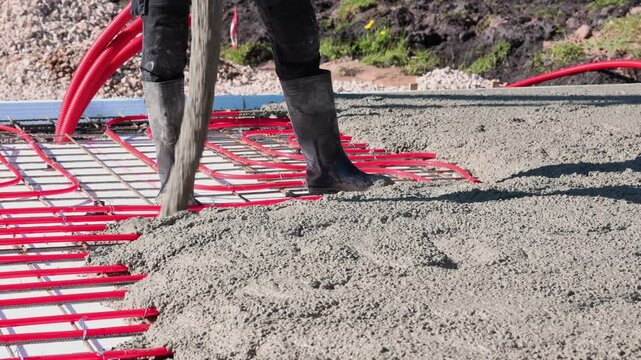 Pouring concrete over underfloor heating system &ndash; construction process Video of a construction worker in rubber boots pouring concrete over red underfloor.