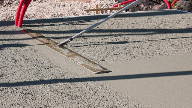 Worker smoothing fresh concrete with trowel close-up footage of a construction worker using a long-handled trowel to level and smooth a freshly.