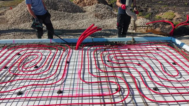 Pouring concrete over underfloor heating system &ndash; construction process Video of a construction worker in rubber boots pouring concrete over red underfloor.
