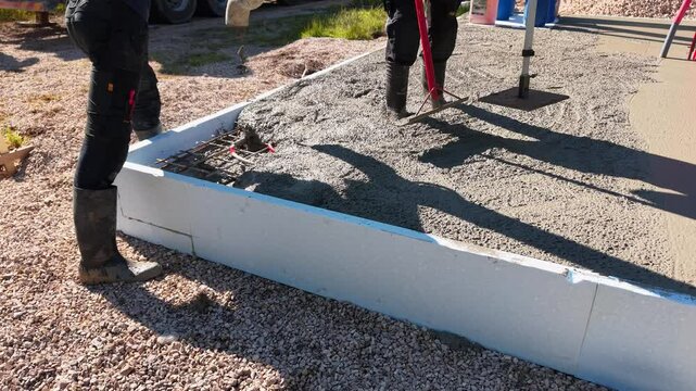 Pouring concrete over underfloor heating system &ndash; construction process Video of a construction worker in rubber boots pouring concrete over red underfloor.