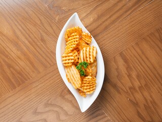 Crispy waffle fries served on white ceramic dish over wooden background