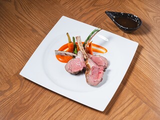 Grilled lamb chops with roasted vegetables and red sauce on a white square plate