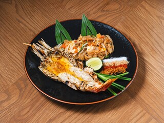 Pad Thai with grilled river prawn served on black plate with traditional Thai condiments