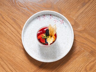 Panna cotta in glass topped with berry sauce and fresh fruits on ceramic plate