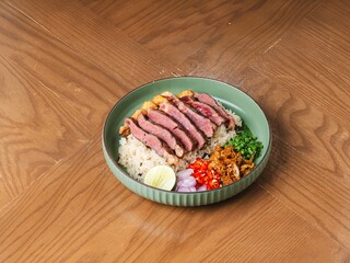 Thai fusion rice dish with grilled wagyu beef, shrimp, chili, and lime on wooden table