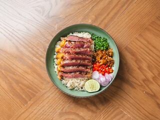 Thai fusion rice dish with grilled wagyu beef, shrimp, chili, and lime on wooden table